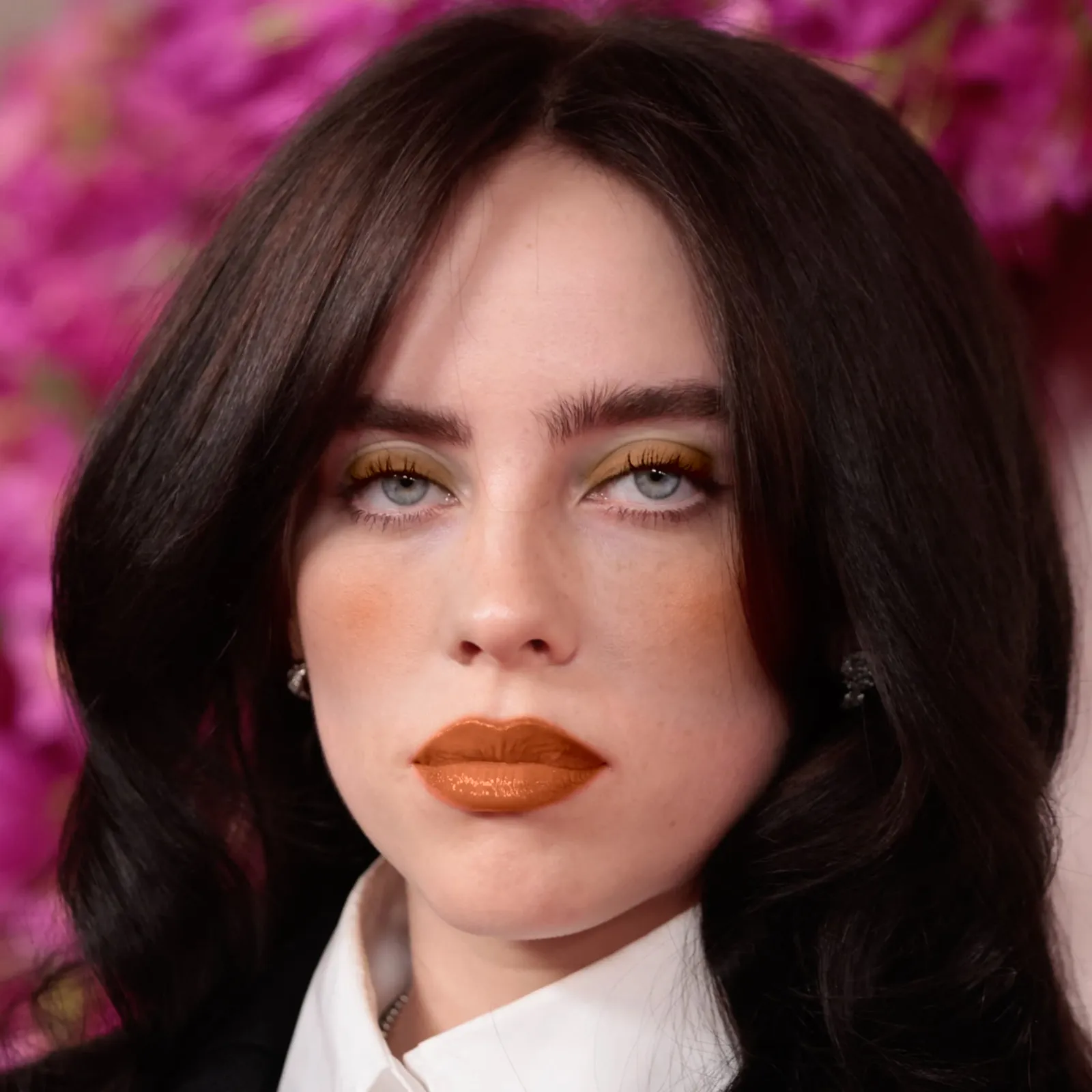 Billie Eilish with warm makeup — olive shadow and burnt orange lip